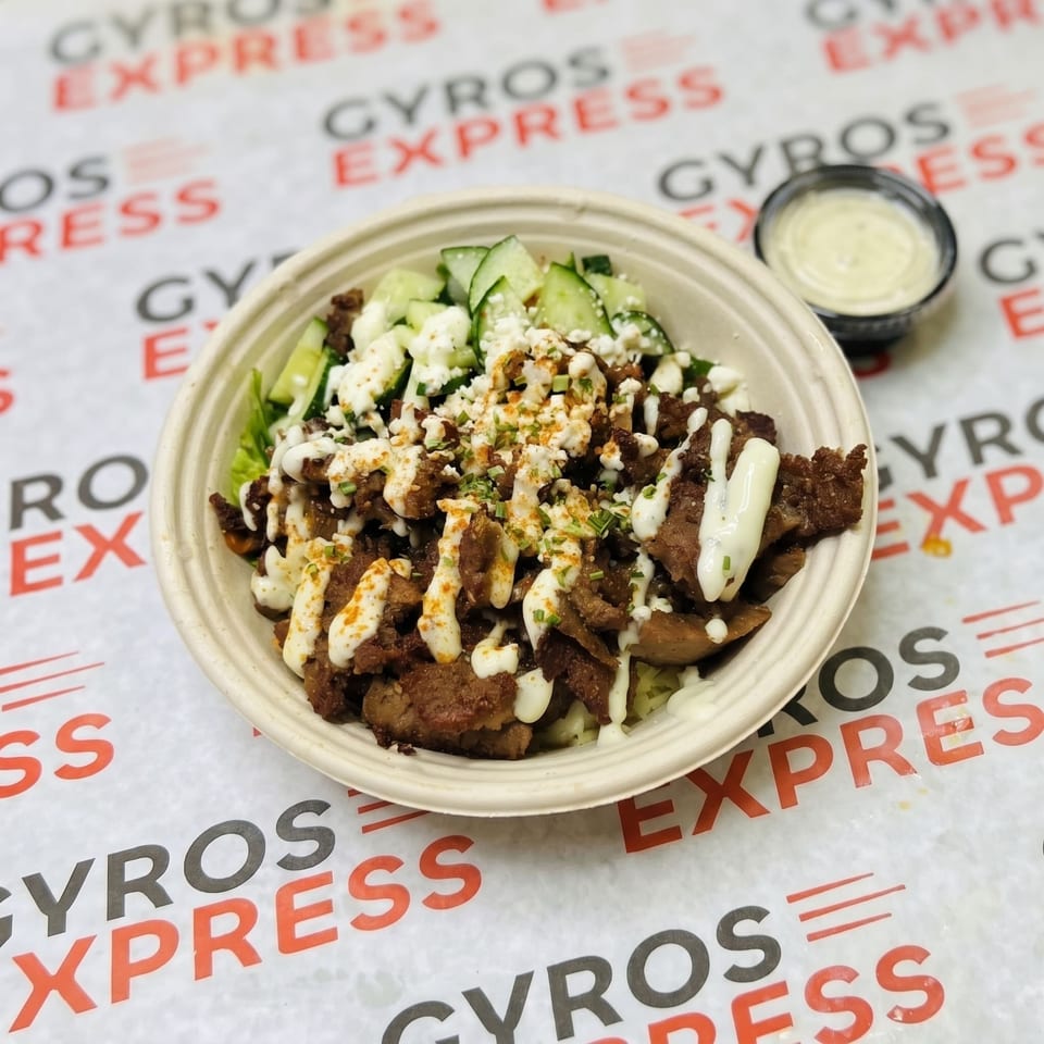 A Gyros Express bowl with meat, cucumbers, feta, and sauce, with a side of dressing.