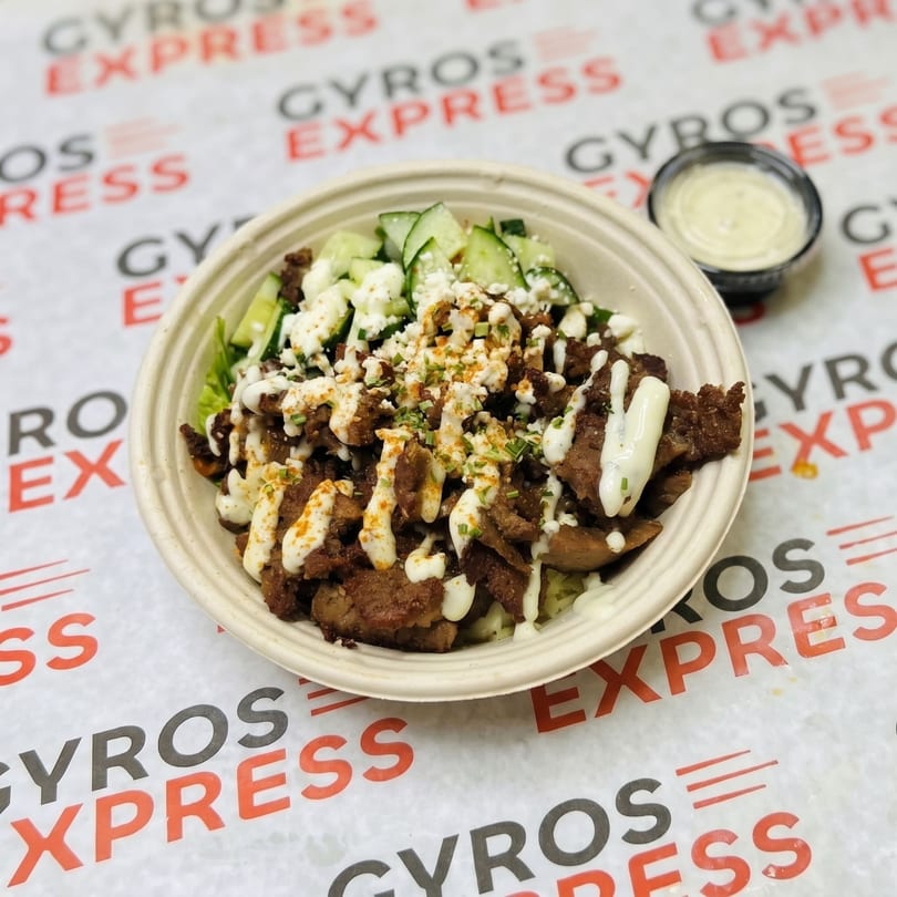 A Gyros Express bowl with meat, cucumbers, feta, and sauce, with a side of dressing.