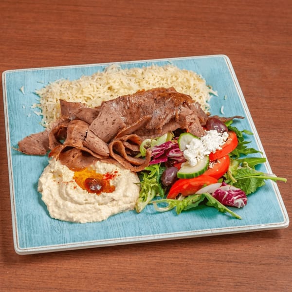 Doner kebab plate with rice, hummus, salad, and sliced meat on a blue plate.
