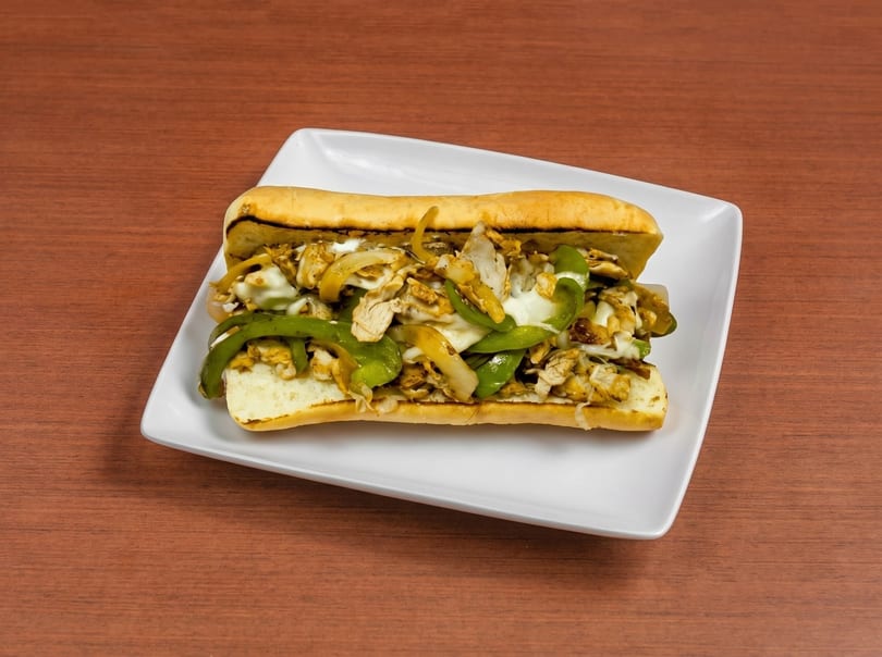 Chicken cheesesteak sandwich with melted cheese, green peppers, and onions on a white plate.
