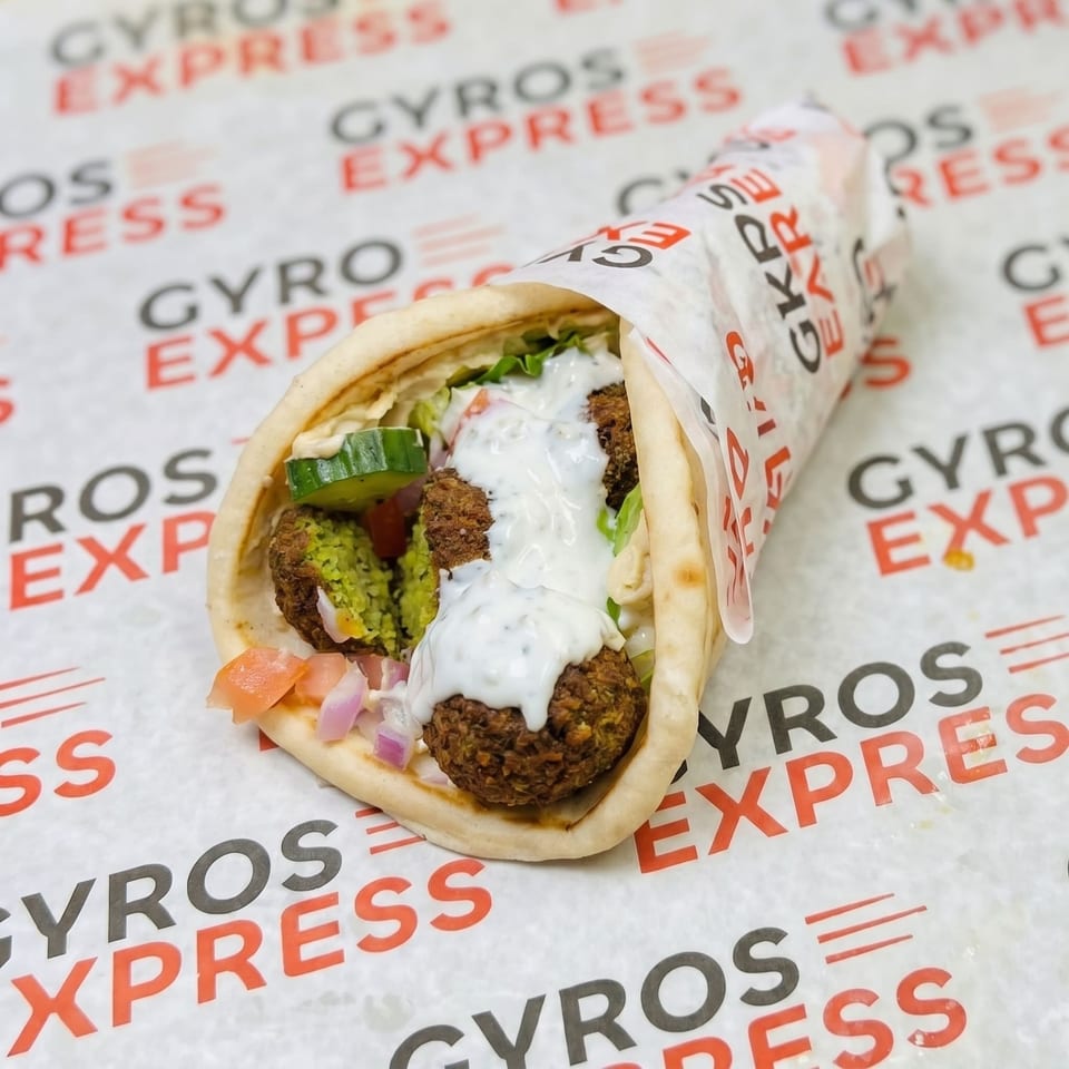 A falafel wrap from Gyros Express, filled with falafel, vegetables, and white sauce, on branded paper.