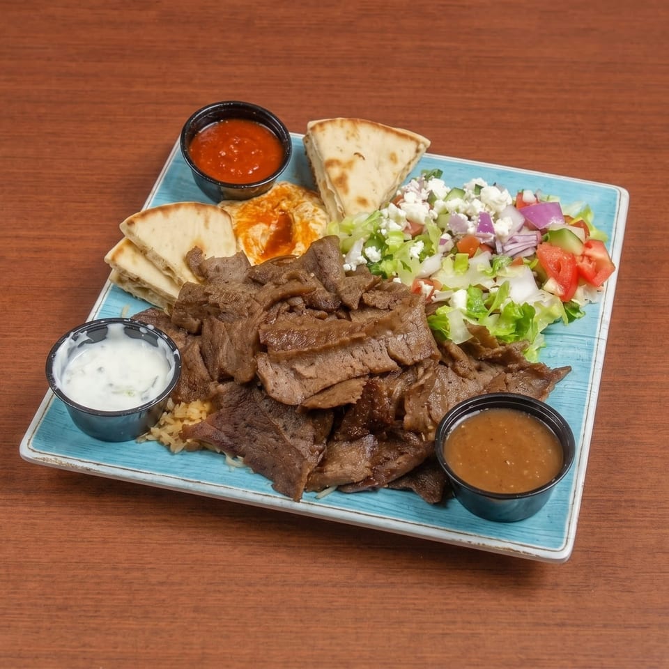 A gyro platter with sliced meat, rice, salad, pita bread, hummus, and sauces on a blue plate.