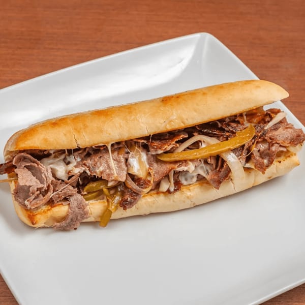 A close-up of a Philly cheesesteak sandwich with melted cheese, onions, and peppers on a white plate.