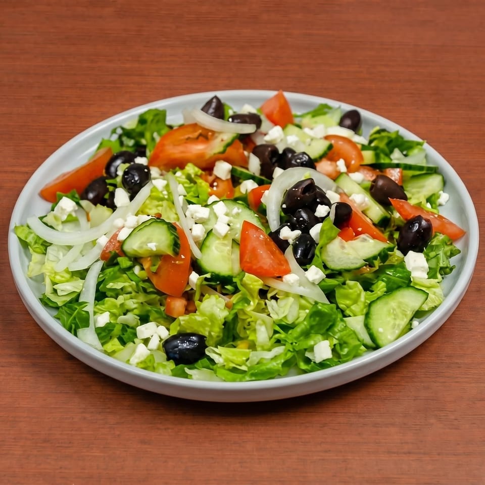 A fresh Greek salad with lettuce, tomatoes, cucumbers, onions, black olives, and feta cheese.