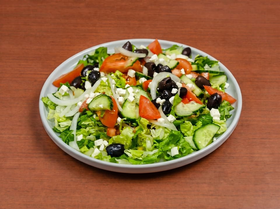 A fresh Greek salad with lettuce, tomatoes, cucumbers, onions, black olives, and feta cheese.