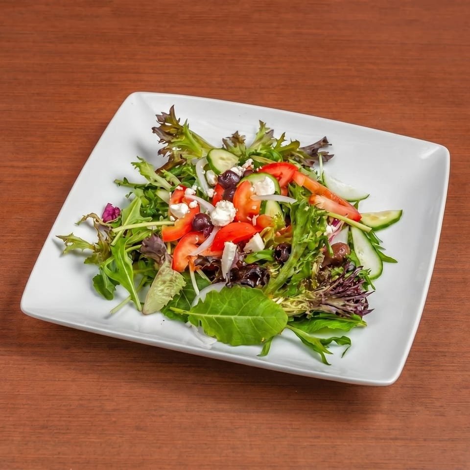 Fresh garden salad with mixed greens, tomatoes, cucumbers, olives, onions, and feta cheese.