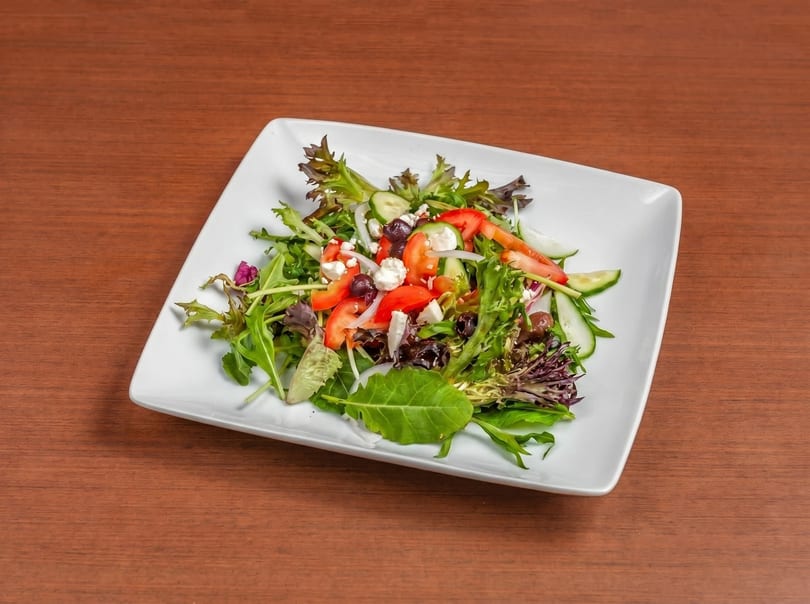 Fresh garden salad with mixed greens, tomatoes, cucumbers, olives, onions, and feta cheese.