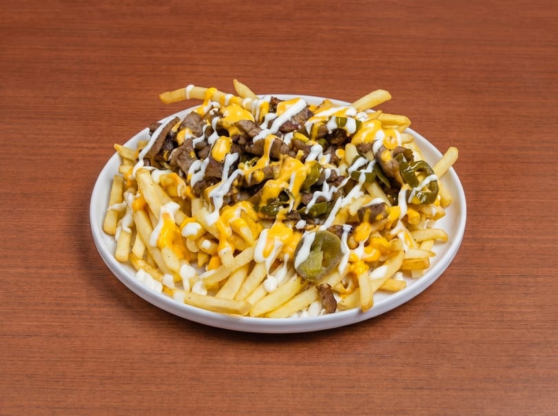 Loaded fries with steak, melted cheese, white sauce, and jalapeños on a white plate.
