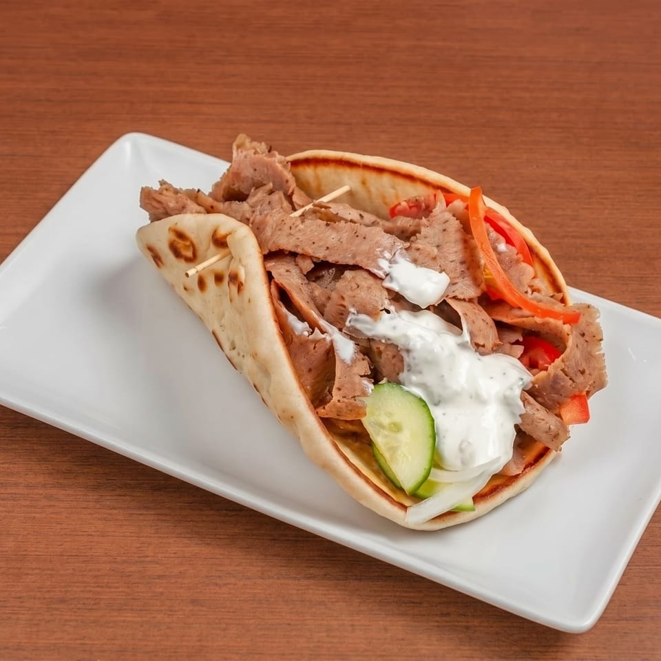 A gyro sandwich with sliced meat, vegetables, and white sauce on a white plate.